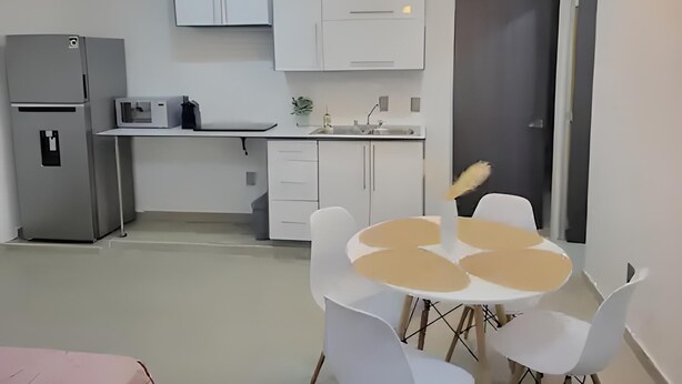 Eine kompakte Küche mit weißen Schränken, einem Kühlschrank, einer Mikrowelle und einem Essbereich mit einem runden Tisch und Stühlen.