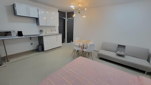 Ein modernes, gut beleuchtetes Zimmer mit Küchenzeile, einem Esstisch mit Stühlen, einer Couch und einem großen Bett.