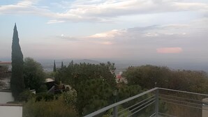 Blick vom Balkon auf eine Stadtlandschaft mit einem markanten Kirchturm, üppigem Grün und fernen Bergen.