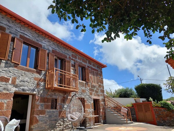 Un bâtiment en pierre avec des volets en bois, un balcon et un fauteuil suspendu à l’extérieur.