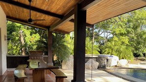 Un patio techado con una parrilla, asientos y una piscina.