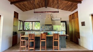 Una cocina con techo de madera, una isla central con taburetes de bar y un salpicadero de azulejos.