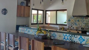 Una cocina con vigas de madera, lámparas colgantes, salpicadero de azulejos y una cesta de fruta.