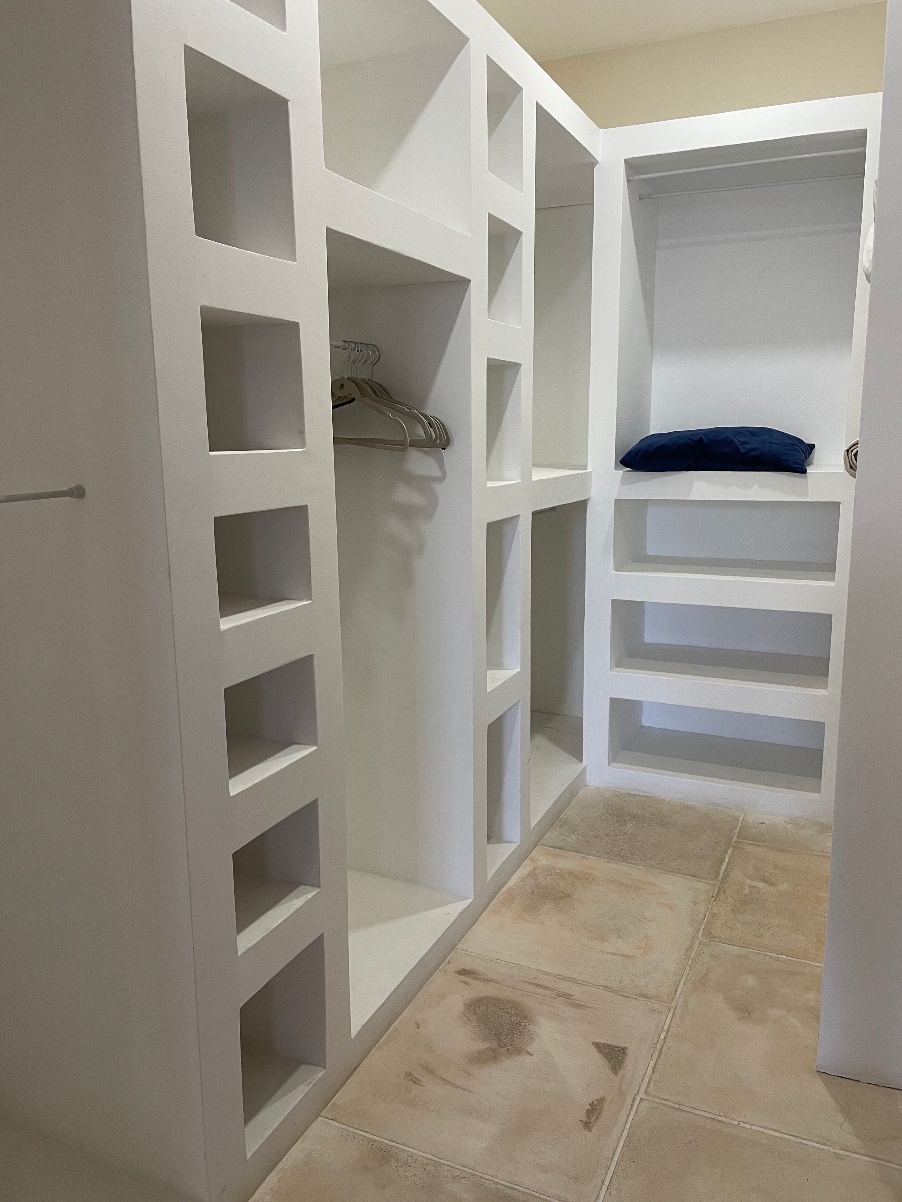 Ein weißer Schrank mit mehreren Regalen und Ablageflächen, ein Fliesenboden und ein Türgriff.