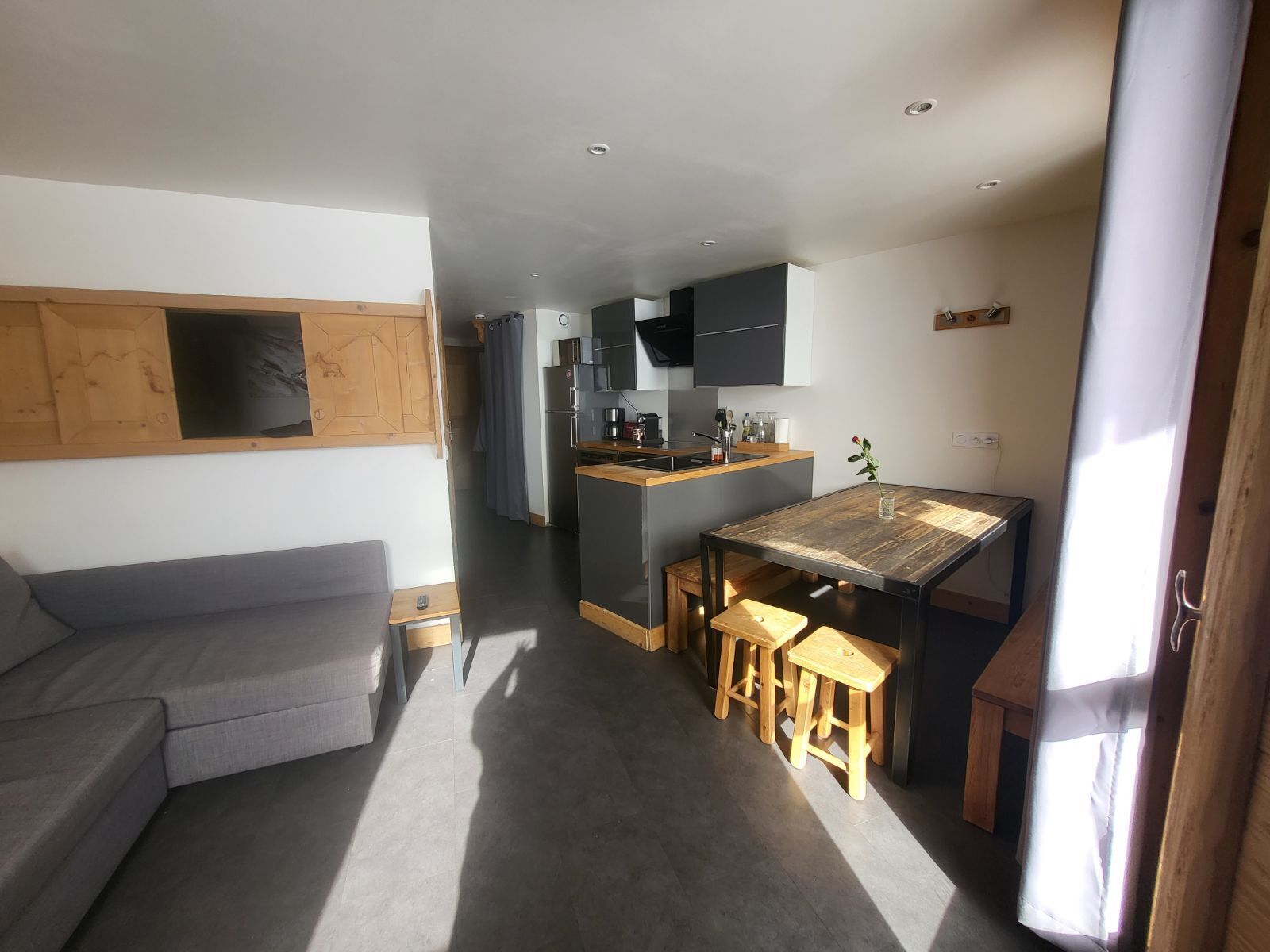 A compact living space with a kitchenette, a grey sofa, and a dining area with stools.