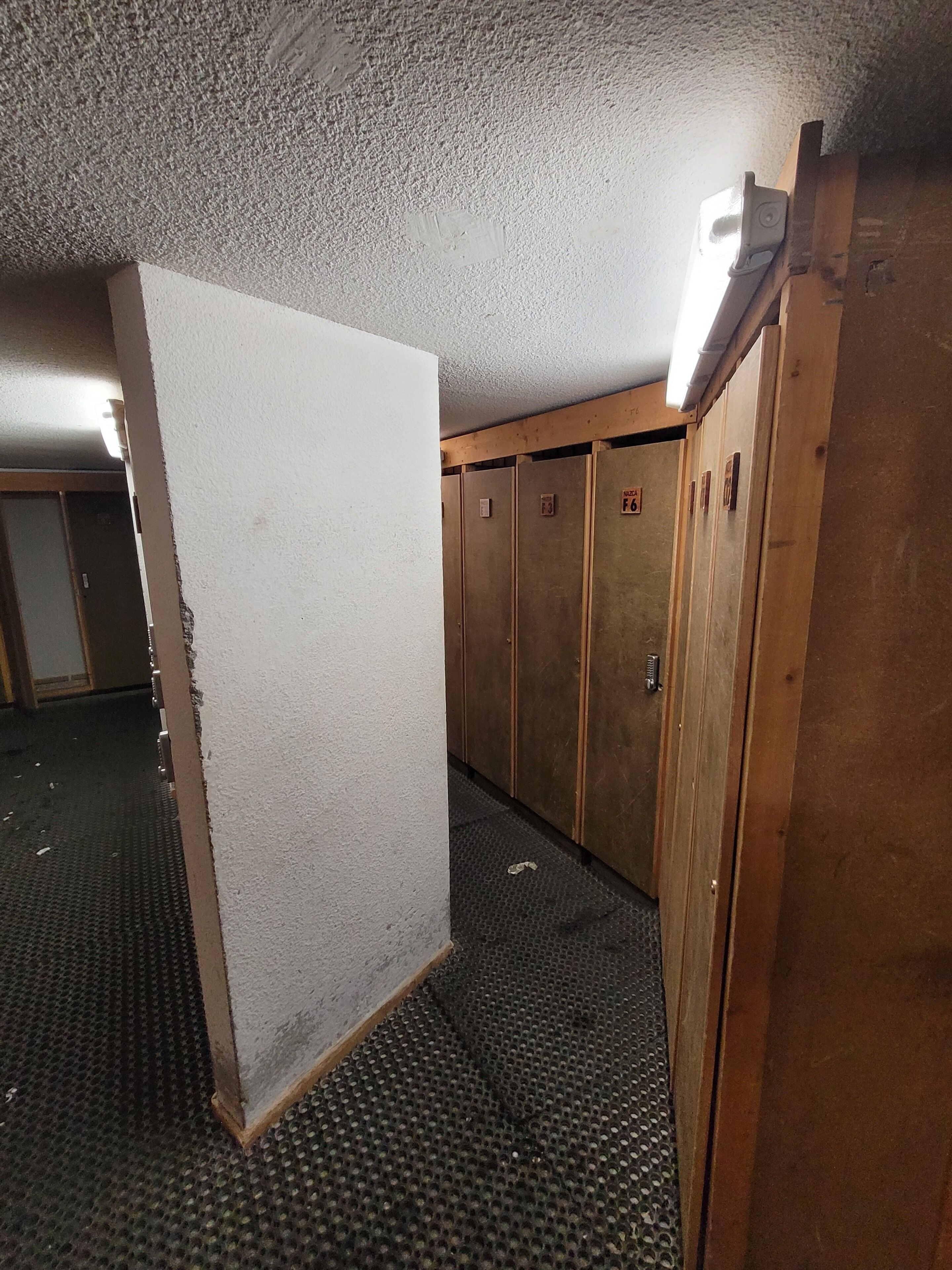 Ein Korridor mit Schließfächern, einer strukturierten Decke und einer teilweise sichtbaren Tür.