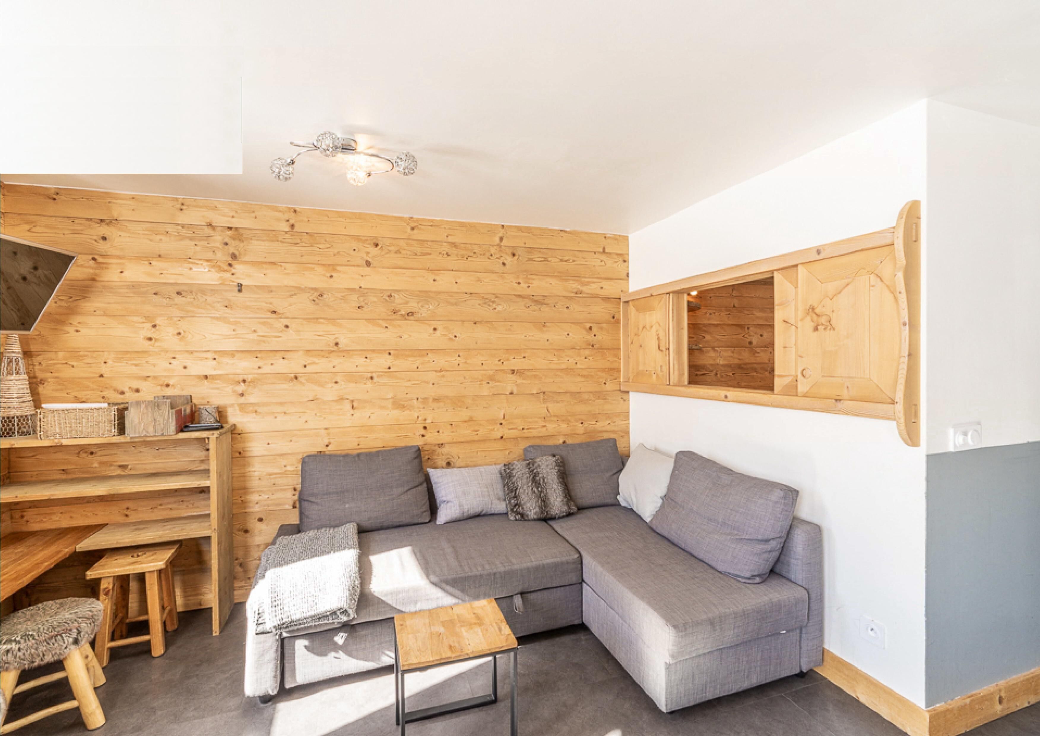 Ein modernes Wohnzimmer mit einer Holzwand, einem grauen Ecksofa, einem Holztisch und einem kleinen Holztisch mit Hockern.