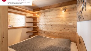 A cozy room with wooden walls, a bed, a window, and a shelf.