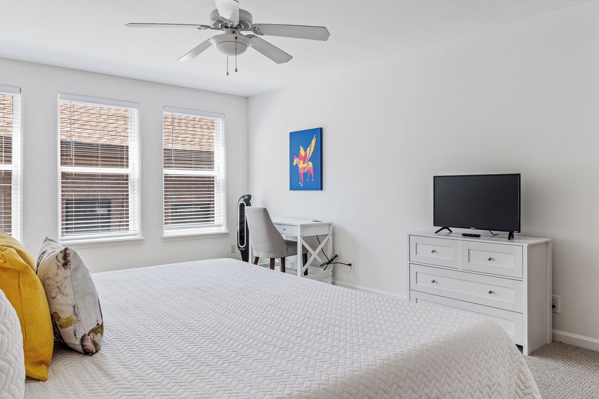 A bedroom with a bed, a desk, a chair, a television, and a ceiling fan.
