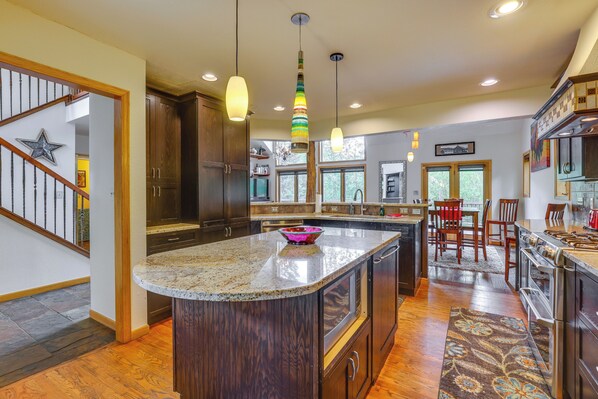 Kitchen with central island, granite countertop, dark cabinets, stainless steel appliances, and large window.