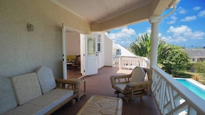 Ein überdachter Balkon mit einer Sitzecke, Stühlen und Blick auf den Pool.