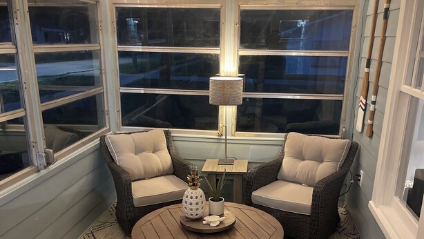 Un rincón acogedor con sillones de mimbre y una mesa redonda, que incluye una lámpara y objetos decorativos.