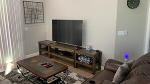 Ein Wohnzimmer mit einem Flachbildfernseher auf einem Holzboden, einem braunen Ledersofa und einem Couchtisch mit Fernbedienungen.