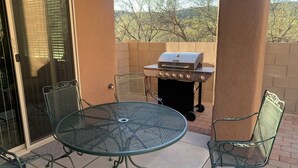 Eine Terrasse mit einem runden Metalltisch und Stühlen, einem Grill und einer Schiebetür.