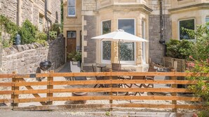 A stone building with a bay window, a wooden gate, and outdoor seating with an umbrella.