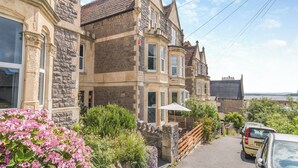 A row of traditional stone houses with bay windows, a paved driveway, and parked cars.