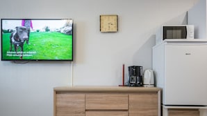Une chambre moderne avec un téléviseur fixé au mur, sur lequel on peut voir un chien, ainsi qu’un meuble en bois, une machine à café et un four à micro-ondes.