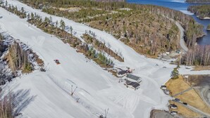 Une piste de ski enneigée, avec un petit chalet et un lac en arrière-plan.