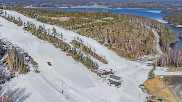 Una pista de esquí nevada con un refugio y un lago al fondo.