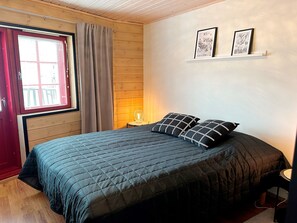 Un dormitorio con una cama, una ventana con persianas, una lámpara y dos cuadros en la pared.
