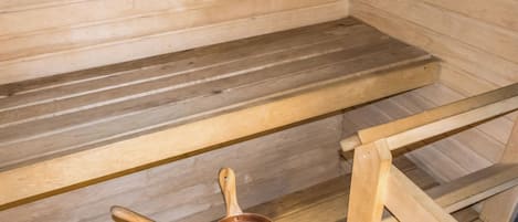 Een sauna met houten banken en een koperen emmer met een schaal.