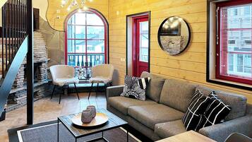 A cozy living room with a stone staircase, a wooden ceiling, a round mirror, and a red door.