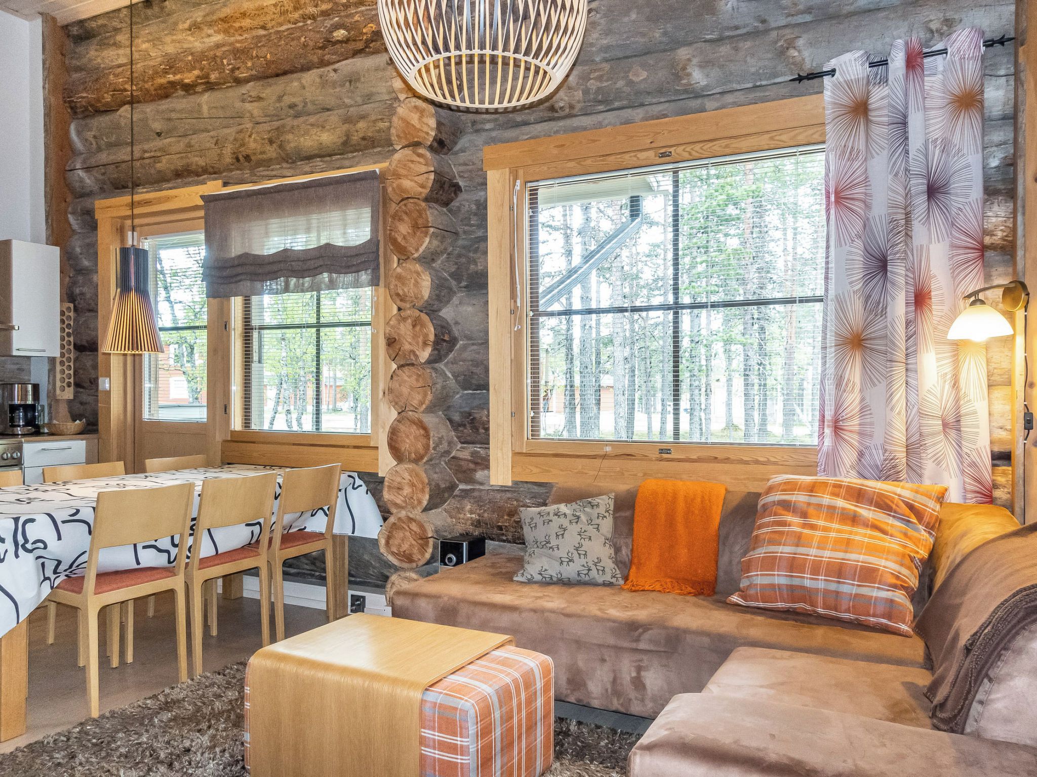 L’intérieur d’une cabane en rondins comprend un coin repas, un canapé avec des coussins et une grande fenêtre avec des rideaux.