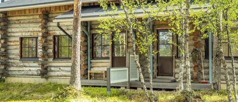 A log cabin with a porch, large windows, and a chimney.
