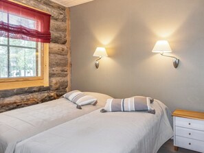 A bedroom with two beds, a nightstand, and a window with blinds.
