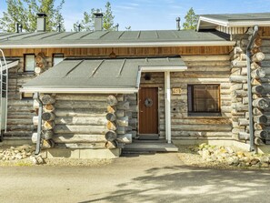 A log cabin with a wooden door, a window with blinds, and a chimney.