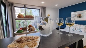 Een eettafel met gebak, een champagnefles en glazen witte wijn in een kamer met een blauwe wand en een raam met gordijnen.