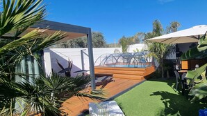 Zwembadgedeelte met een houten terras, een overdekte hottub en een beschut zithoekje met parasols.