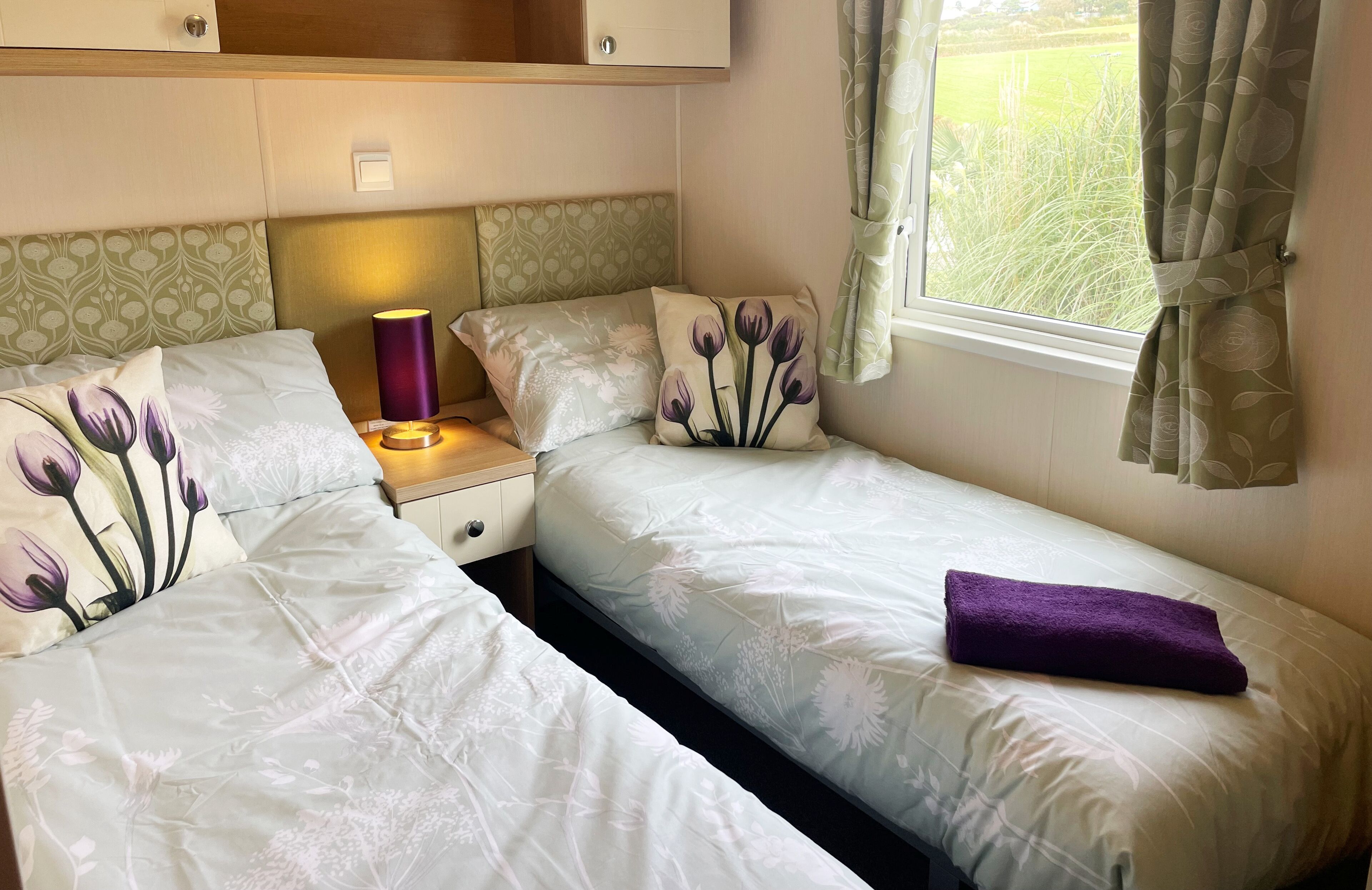 A bedroom with two beds, a bedside table with a lamp, and a window with curtains.