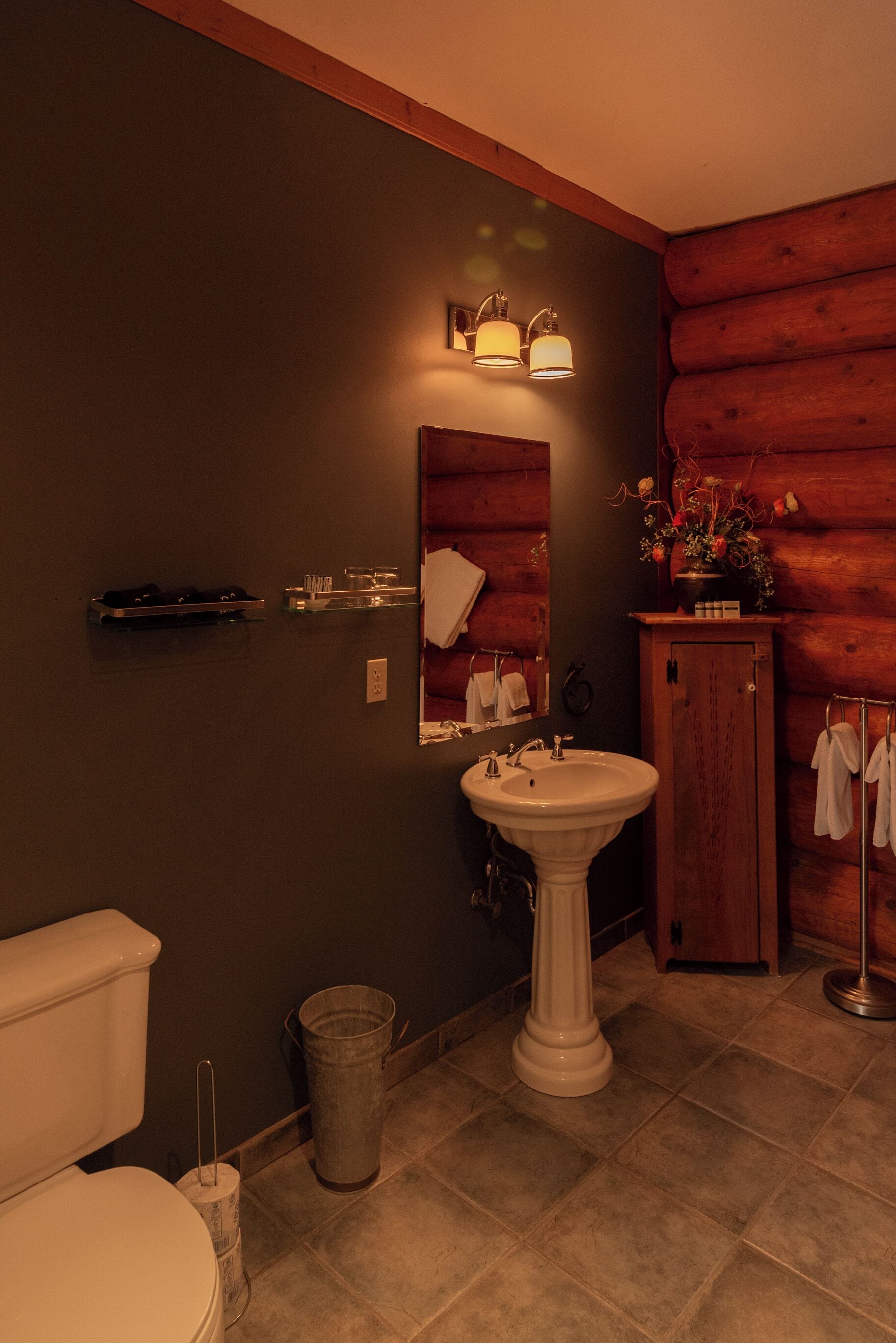 A bathroom with a pedestal sink, wooden wall paneling, a mirror, and a small cabinet with towels.