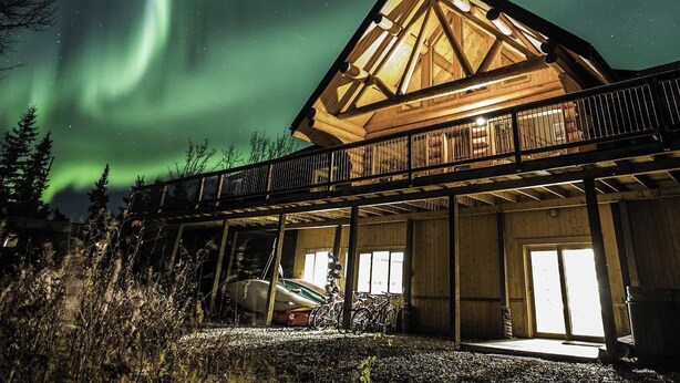 Une cabane dotée d’une grande véranda ouverte, de poutres en bois et offrant une vue sur les aurores boréales.