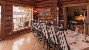 Un intérieur en bois avec une longue table à manger, des chaises, un lustre et une grande fenêtre.