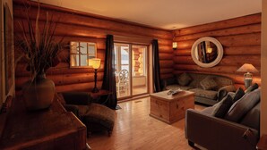 L’intérieur d’une cabane en rondins, avec un plancher en bois, un canapé, une table basse, une lampe et un vase contenant des plantes séchées.