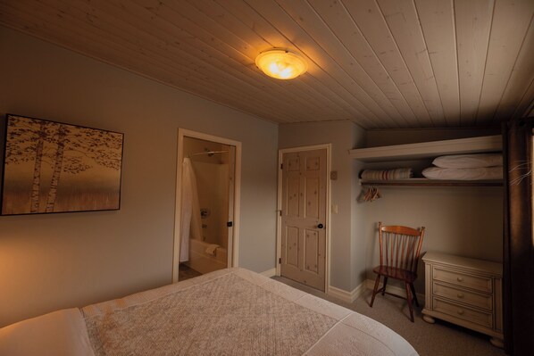 Un dormitori amb llit, sostre de fusta, porta, cadira i un armari.