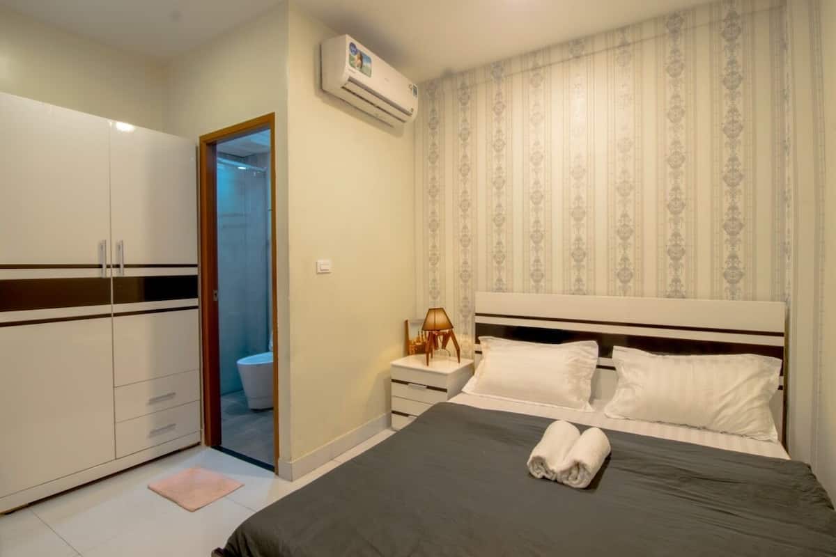 A bedroom with a bed, a wardrobe, a nightstand, and an air conditioning unit.