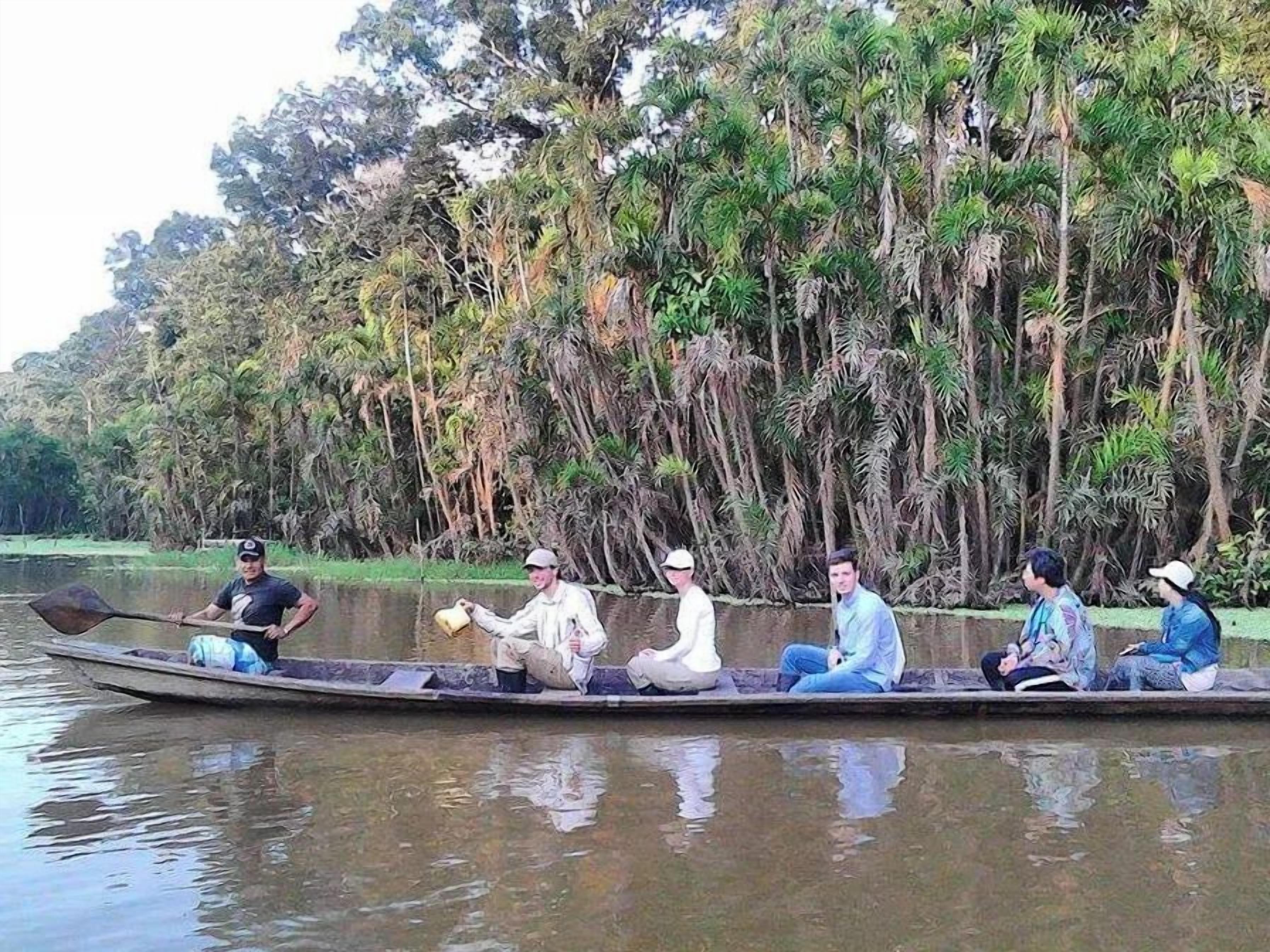 Un groupe de personnes se trouve à bord d’un long bateau naviguant sur une rivière paisible, entouré d’une végétation tropicale luxuriante.