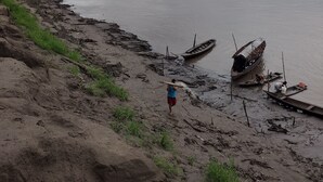 A riverbank with boats and a person carrying a long object. - Iquitos (San Juan Bautista)