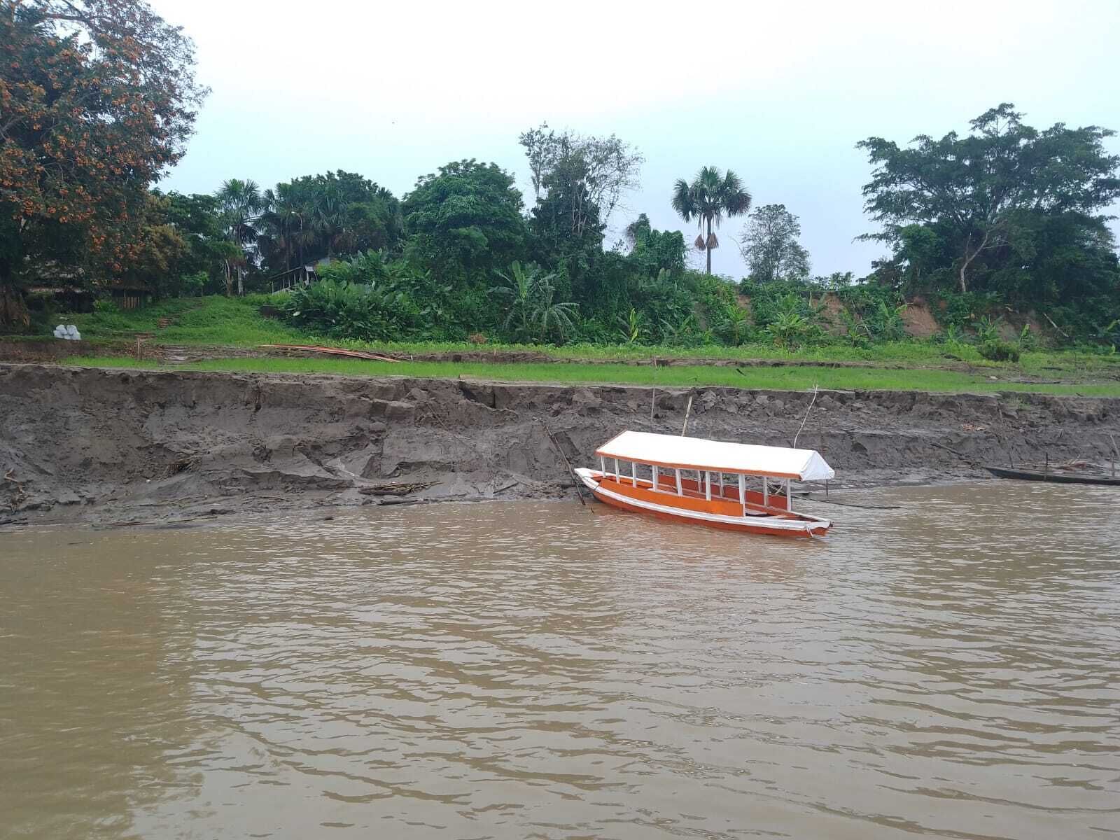 A boat on a river with a grassy embankment and trees in the background.