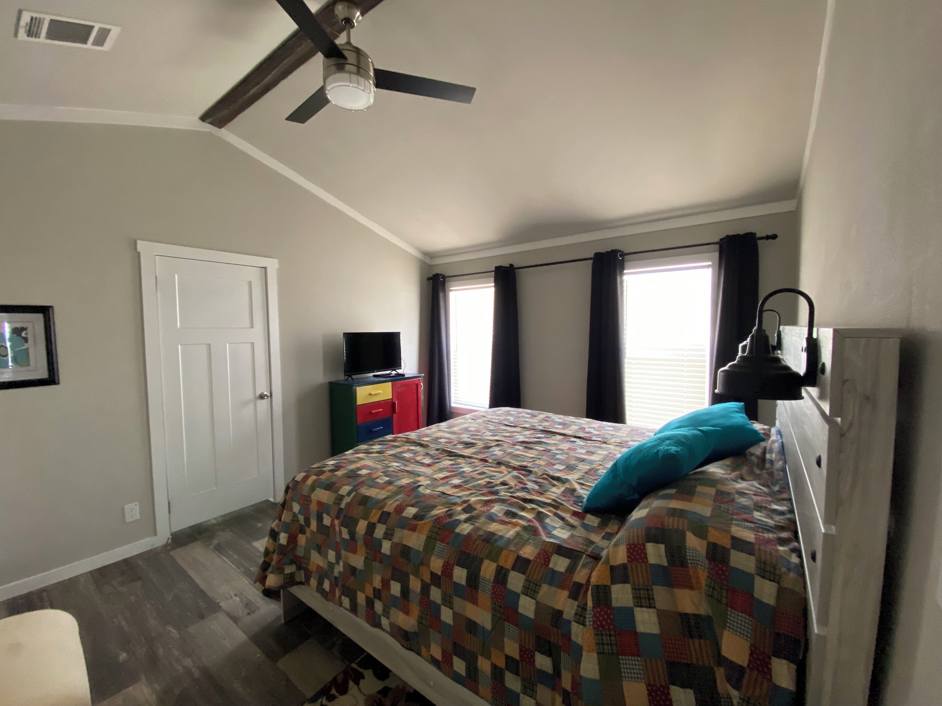 A bedroom with a bed, a ceiling fan, a TV on a cabinet, and a window with curtains.