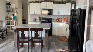 A modern kitchen with white cabinets, a black refrigerator, and a central island with two chairs.