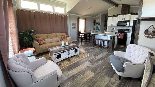 A spacious living room with a high ceiling, a dining area, and a kitchen with white cabinets and a black refrigerator.