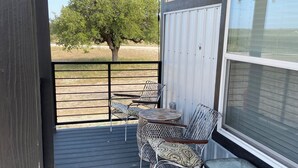 A covered outdoor area with a table and chairs, a large window, and a view of trees and a fence in the background.