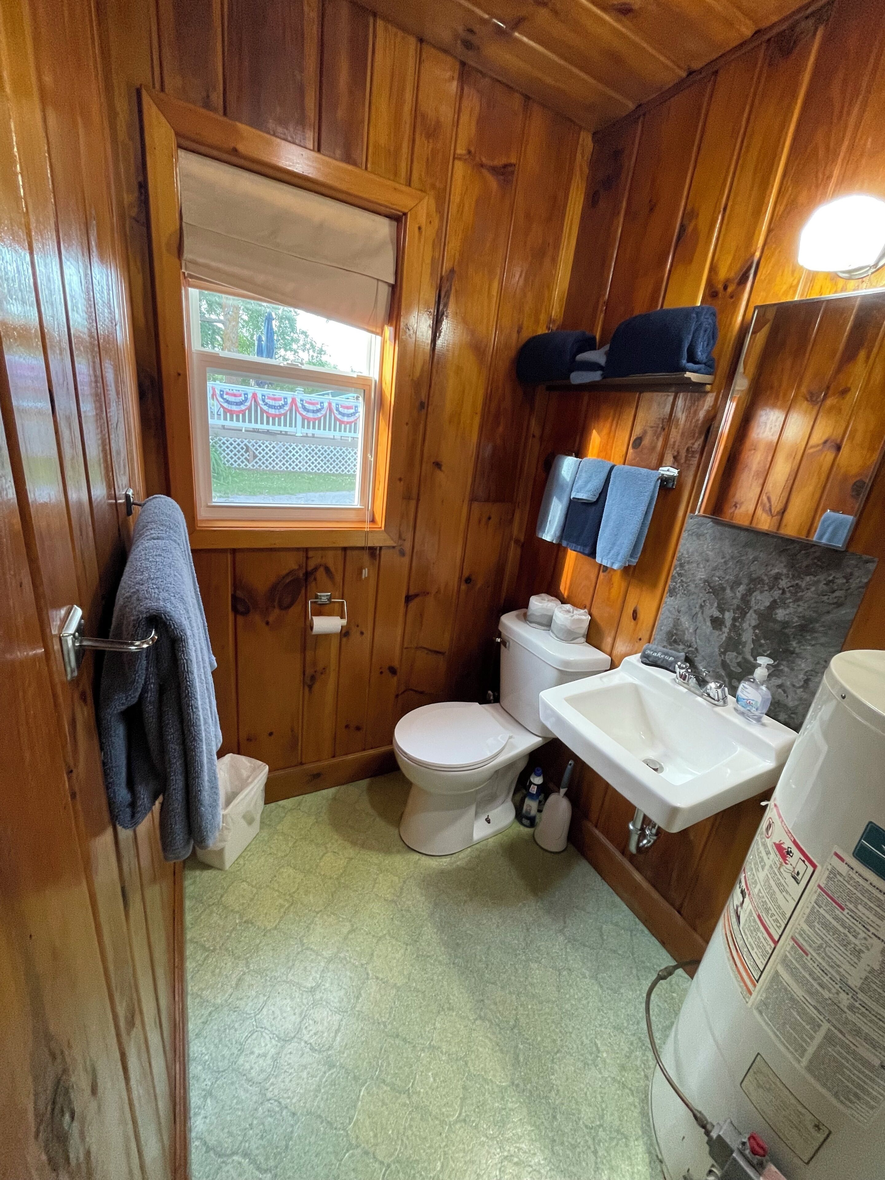 A wooden-paneled bathroom with a toilet, sink, and window.