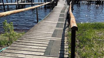 Un muelle de madera que se adentra en un cuerpo de agua, con una zona de césped en un extremo y un cielo despejado.