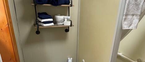 Een badkamer met een toilet, een douchecabine, een plank met handdoeken en een toiletborstel.