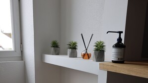 A corner of a room with a white wall, a wooden shelf, and a window.